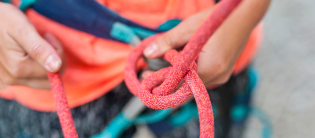 A close up of a climbing Instructor's hands and a pink climbing rope whilst teaching tying-in with a figure eight knot.