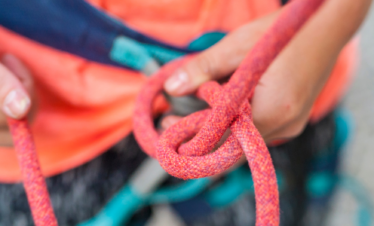 A close up of a climbing Instructor's hands and a pink climbing rope whilst teaching tying-in with a figure eight knot.